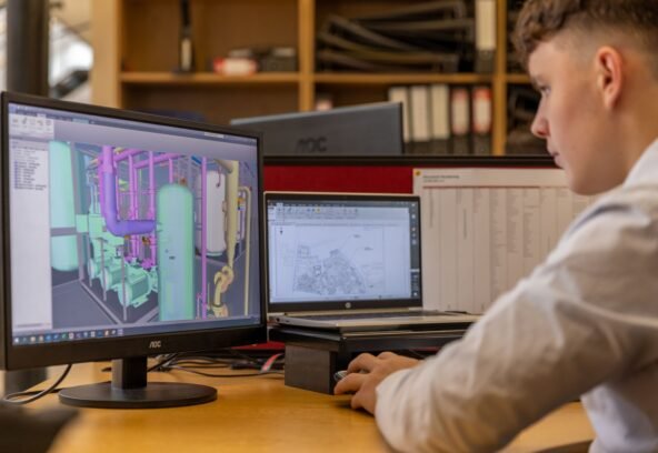 Engineer working with CAD software on dual monitors in an office setting.