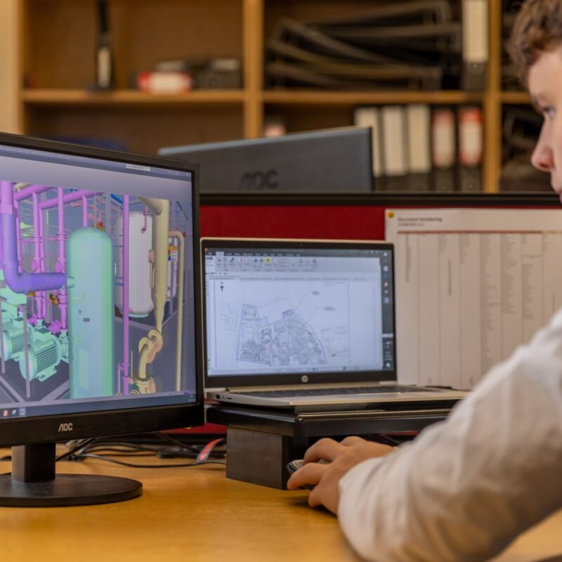 Engineer working with CAD software on dual monitors in an office setting.