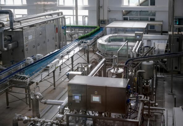 Interior view of an automated beverage bottling factory with machinery and conveyor belts.