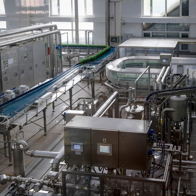 Interior view of an automated beverage bottling factory with machinery and conveyor belts.