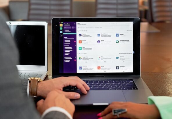 Two professionals collaborating using laptops and communication software in a business setting.