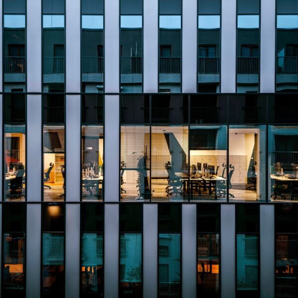 Illuminated office inside a modern glass building exterior, showcasing architecture and workspace design.