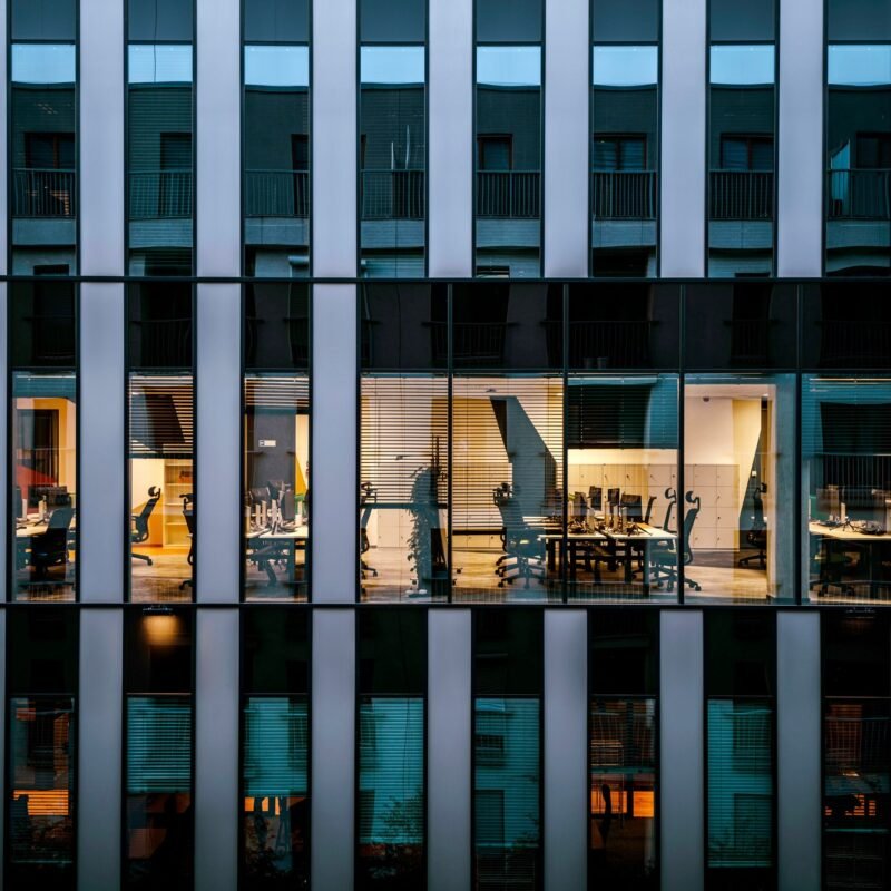 Illuminated office inside a modern glass building exterior, showcasing architecture and workspace design.