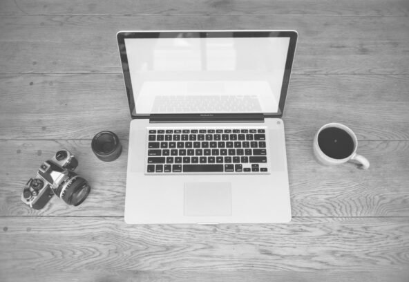 pexels-265144 Monochrome image of a laptop, camera, lens, and coffee cup on a wooden desk