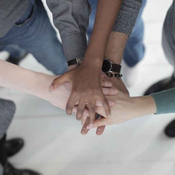 Crop from above of faceless multiracial friends in casual clothes uniting hands after coming to agreement while standing on light grey ceramic floor