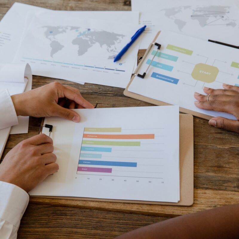 Top view of colleagues discussing charts and graphs on a wooden table during a business meeting.